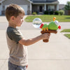 A young boy holds an ant-shaped water blaster toy with a clear sphere on a string in a sunny outdoor setting.