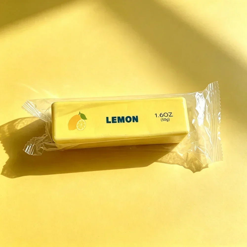 A yellow lemon-shaped squishy fidget toy in a clear plastic bag is shown on a bright yellow surface.
