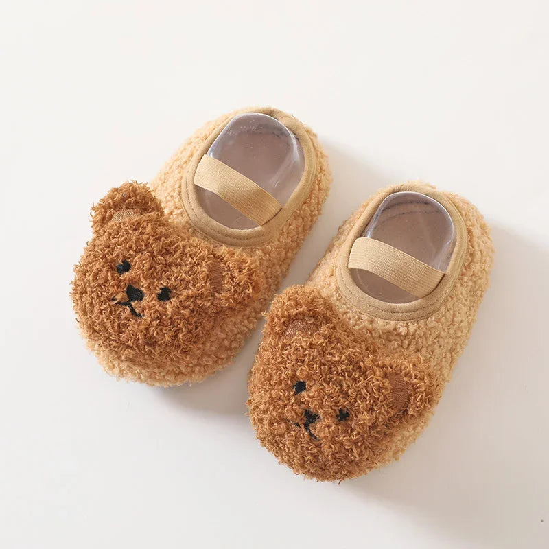 A pair of adorable cartoon bear baby booties made of soft, warm, fuzzy brown material with a clear window.