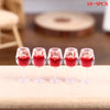 Five miniature resin wine bottles and cups in red color arranged on a wooden surface.