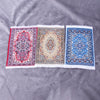 Three miniature handwoven Turkish style carpet mats in red, beige, and blue displayed on a gray fabric.