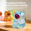 A clear blue glitter capybara squishy toy with a purple nose, shown next to measuring guides.
