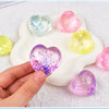 A hand holds a white heart-shaped squishy toy filled with glittery, translucent foam in various colors.