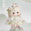 A white collectible figurine of a girl with pink ears and light blonde hair, dressed in a white dress, standing on a decorati