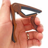 A hand holds a rosewood guitar capo with five picks for acoustic and electric guitars.