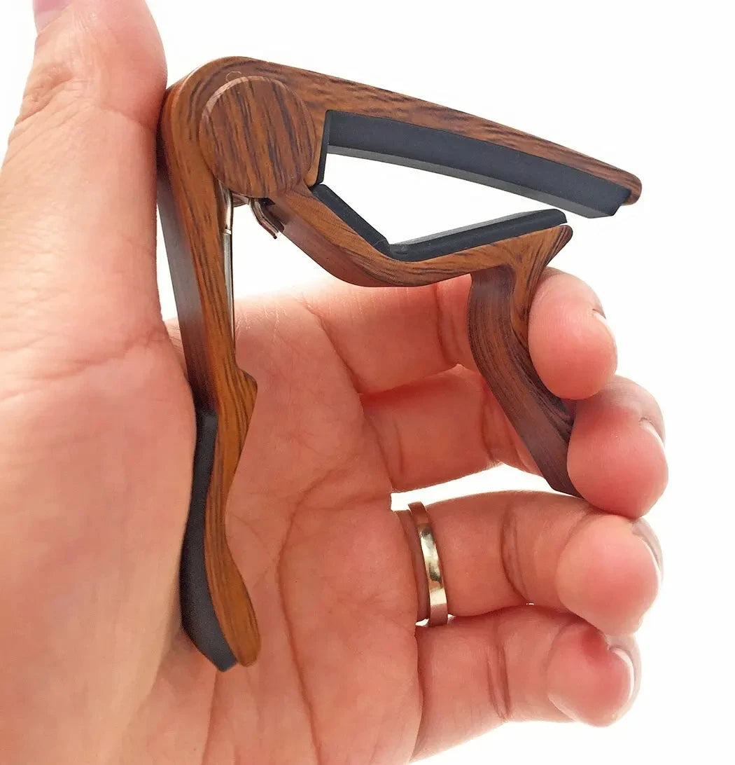 A hand holds a rosewood guitar capo with five picks for acoustic and electric guitars.