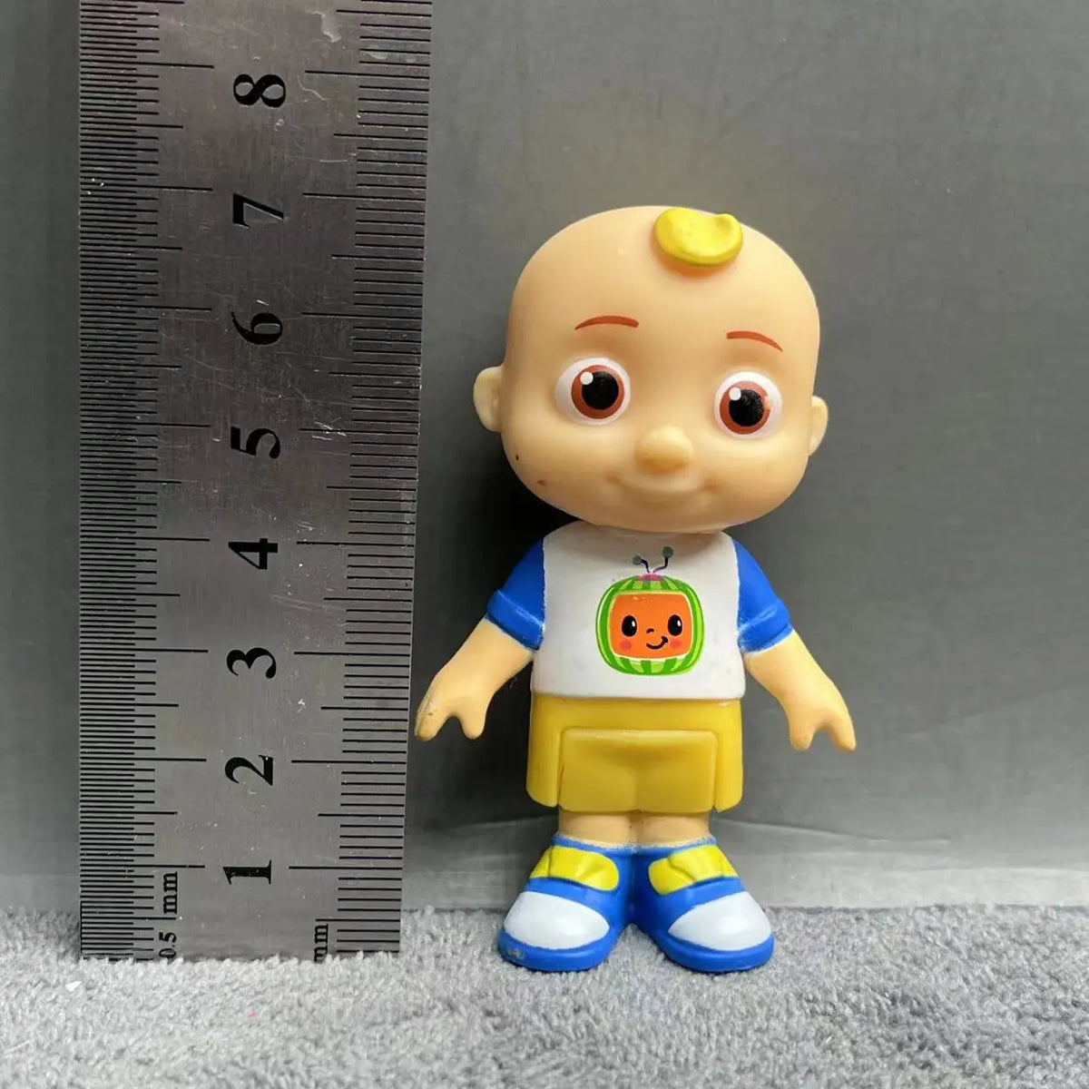 A playful cartoon PVC figurine of a child with a watermelon school bus design on their shirt and yellow pants.