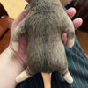 A brown, lifelike skeleton plush toy resembling a dog or cat is held in a person's hand.