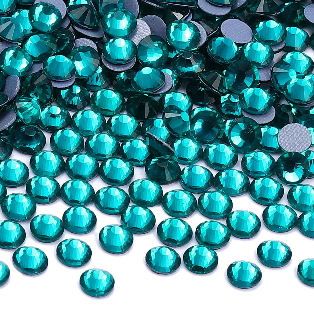 A close-up view of iridescent teal glass crystal rhinestones scattered on a white background.