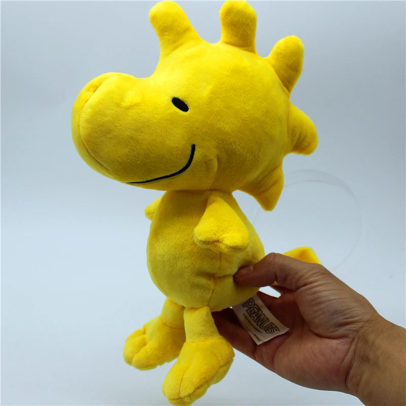 A yellow Peanuts Snoopy plush toy doll being held in a person's hand.