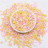 A bowl filled with colorful polymer clay slice sprinkles in pink and yellow scattered on a white surface.
