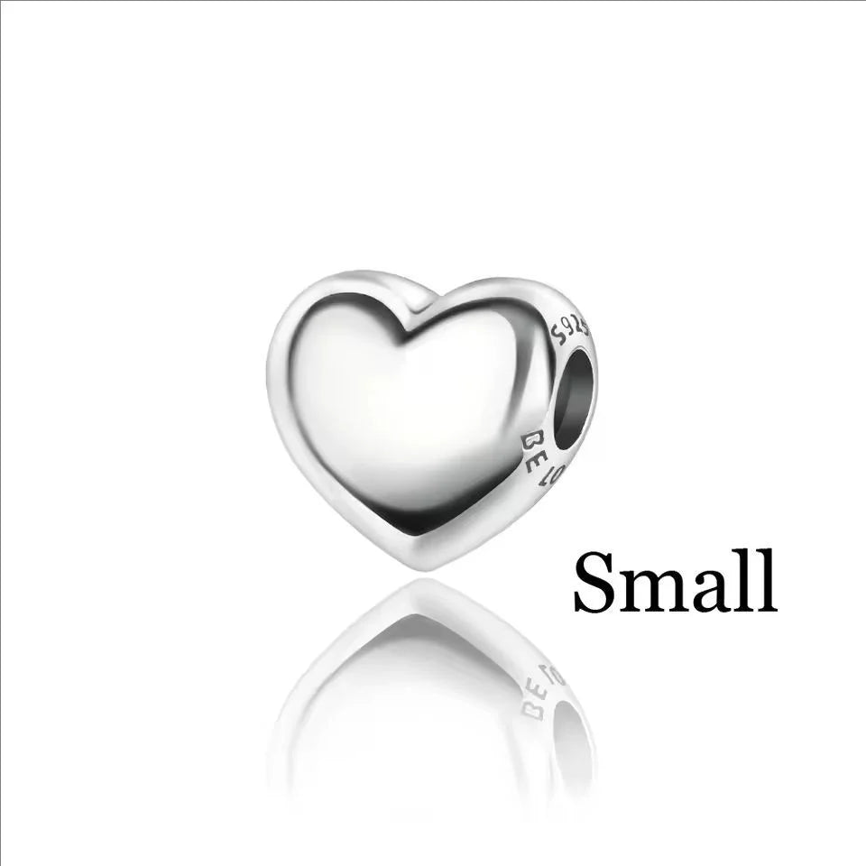 A small, polished silver heart charm with an engraving on the side.