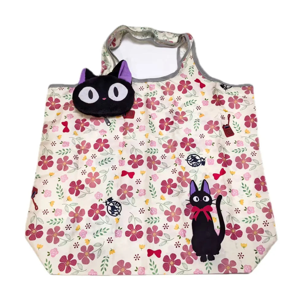 A white fabric tote bag featuring a floral pattern and decorated with black cat plush toys.