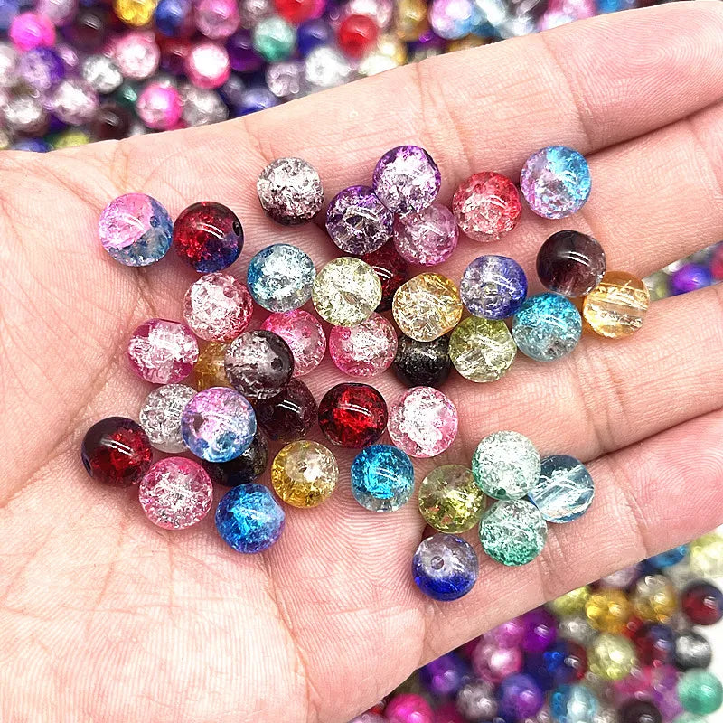 A hand holds a collection of round glass crackle beads in various colors and shades for jewelry making