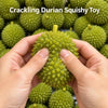 Hands holding a green crackling durian squishy toy with a yellow stem