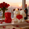A white silicone candle mold shaped like a bear with red ears and a red rose flower, set near red roses and a bottle at sunse