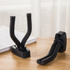 A black wall-mounted guitar holder with a non-slip cradle resting on a wooden surface.