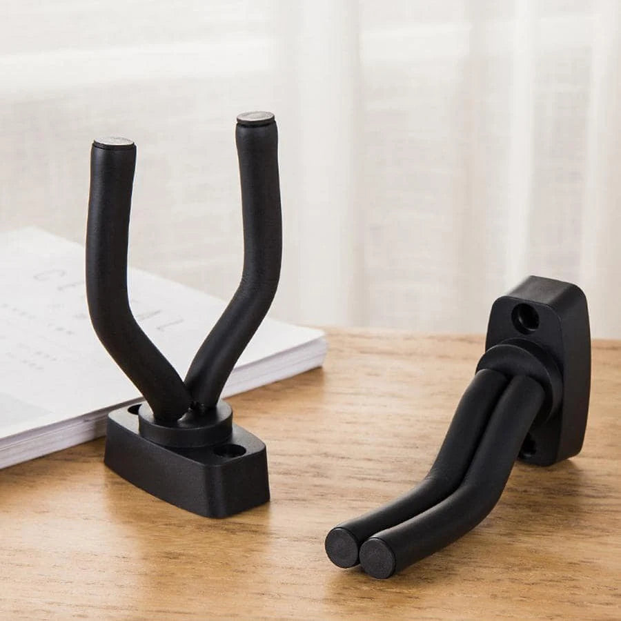 A black wall-mounted guitar holder with a non-slip cradle resting on a wooden surface.