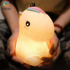 A hand is holding a glowing unicorn LED night light with a pink horn and a light yellow body.