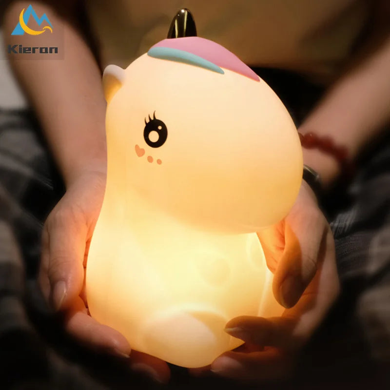 A hand is holding a glowing unicorn LED night light with a pink horn and a light yellow body.