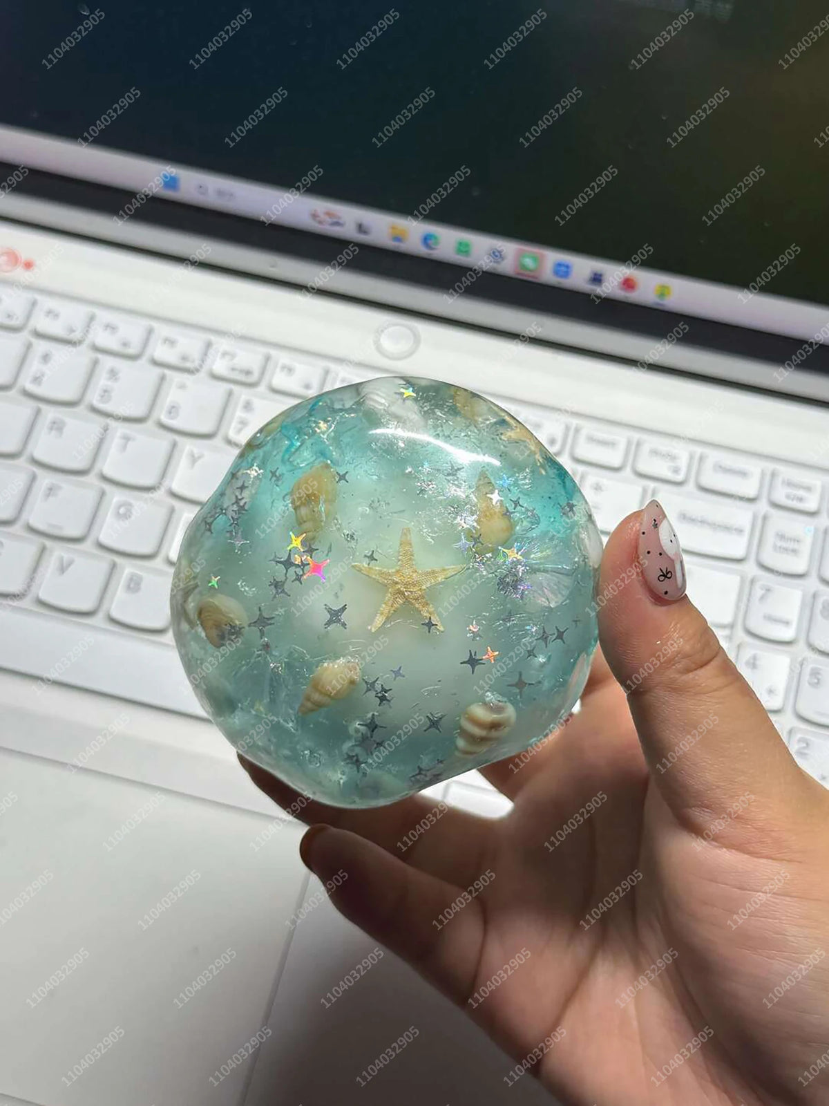 A clear, translucent blue glass stress ball filled with small shells and glitter resting on a laptop keyboard.