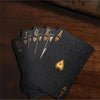 A stack of dark gray frosted poker playing cards showing the Ace through Ten, resting on a wooden surface.