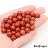 A hand holds a cluster of reddish-brown round jasper beads for jewelry making.