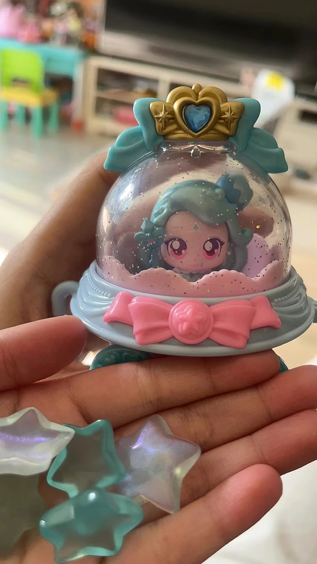 A hand holds a Teenieping Shining Meteor Aurora doll featuring a translucent body, pink bow, and gold crown.