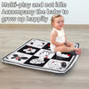A happy baby sitting on a black and white play mat featuring various animal shapes and toys.