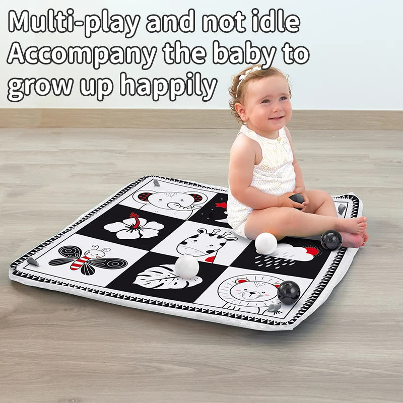 A happy baby sitting on a black and white play mat featuring various animal shapes and toys.