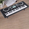 A black 37-key electronic keyboard with a microphone rests on a wooden surface.