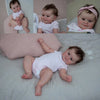 A photo of a lifelike reborn baby doll named Maddie with soft body and detailed 3D skin lying on a white surface.