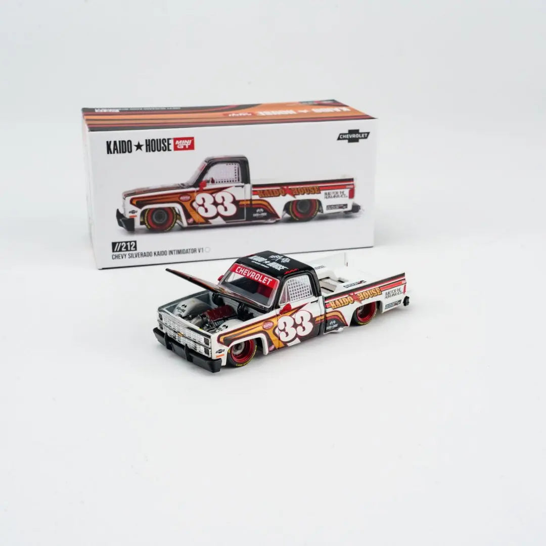 A die-cast model of a 1980s Chevrolet Silverado truck in orange and white, displayed next to its packaging.