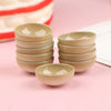 A set of ten miniature beige rice bowls arranged in a stack on a pink surface.