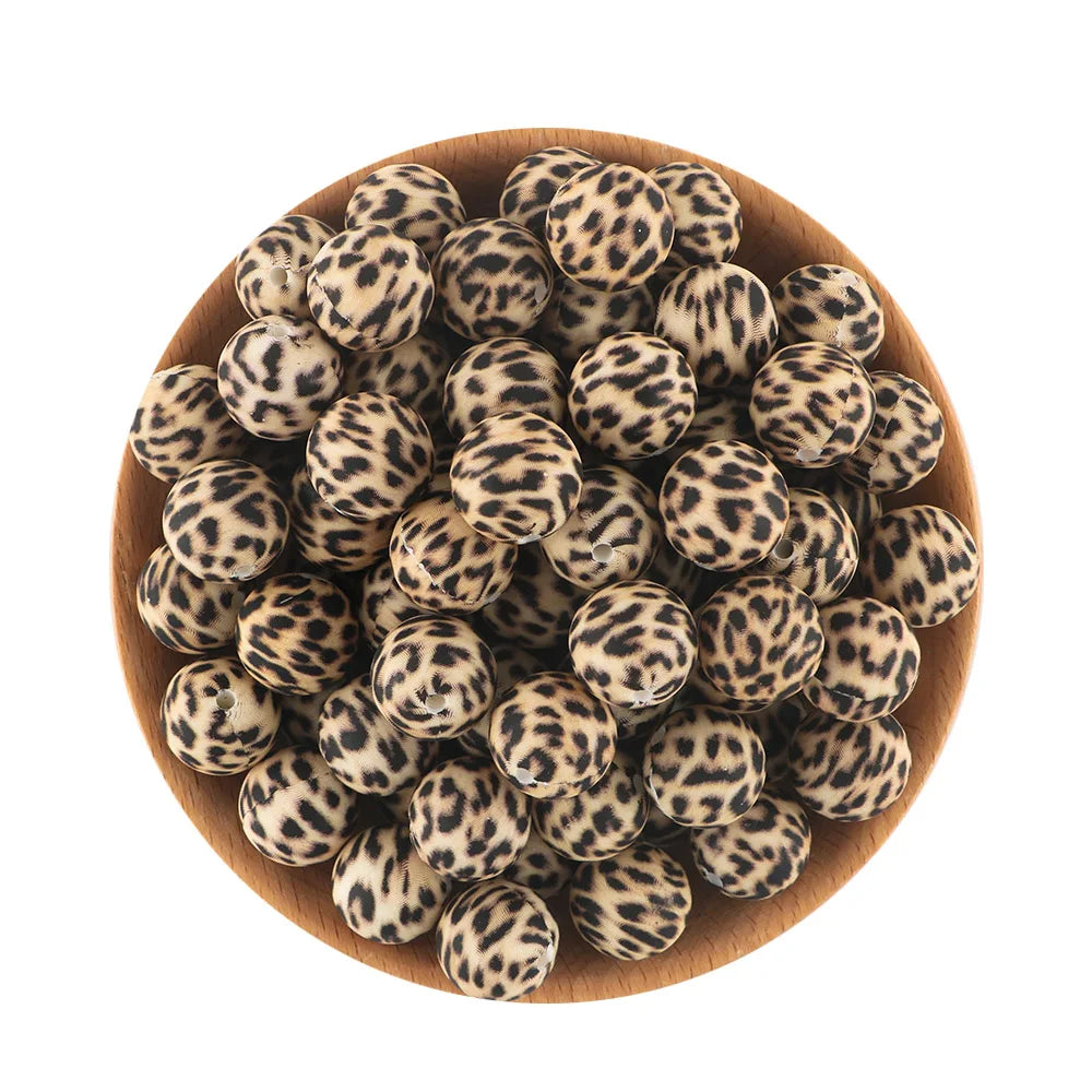 A pile of small, round, black and tan patterned silicone beads for jewelry making in a wooden bowl.