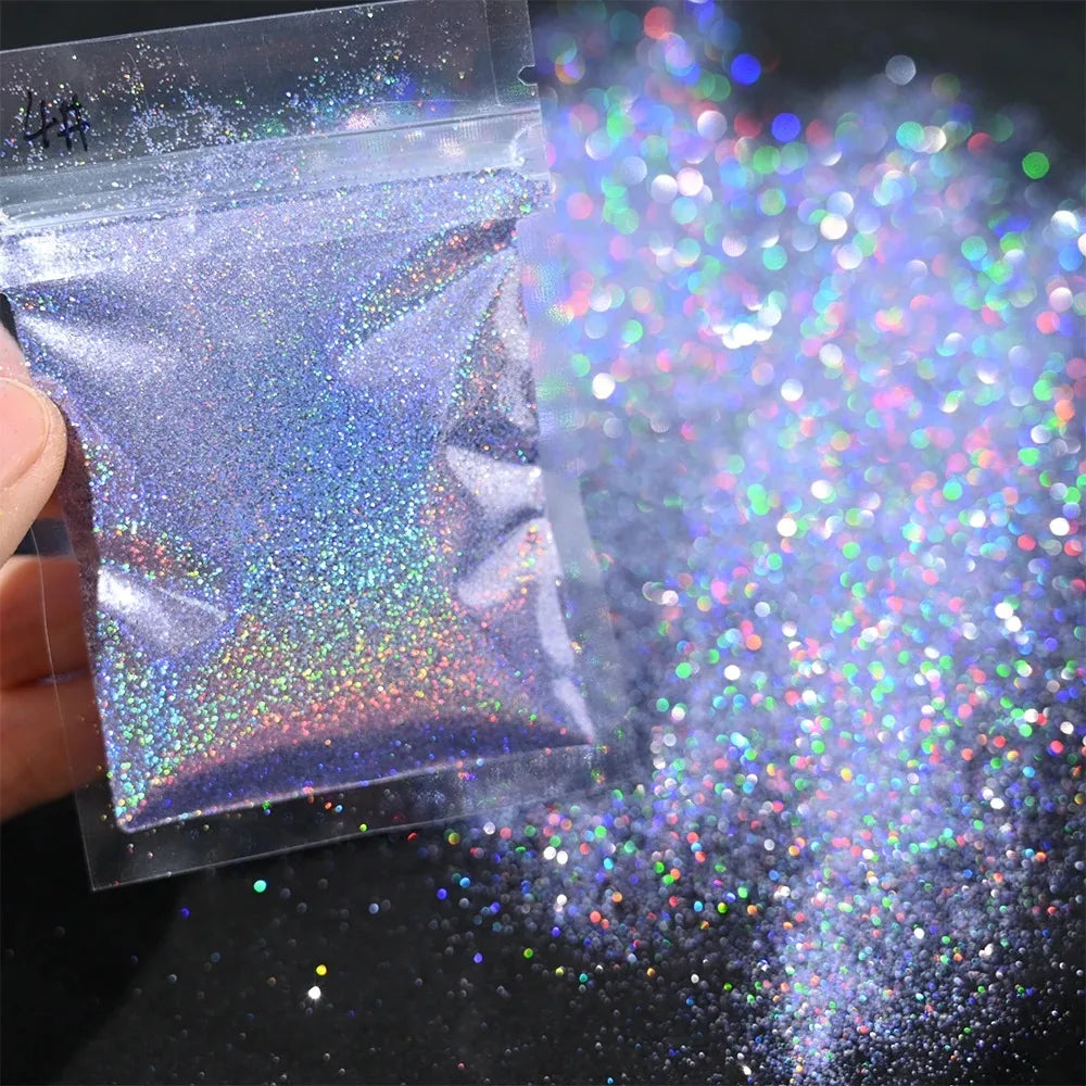 A small plastic bag of holographic rainbow nail glitter is open, with fine sparkle dust scattered on a dark surface.