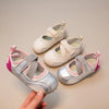 A hand holds a pair of silver and pink girls' casual slip-on shoes with breathable PU upper.