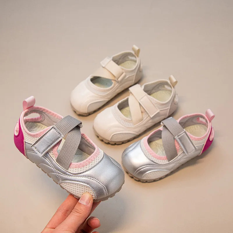 A hand holds a pair of silver and pink girls' casual slip-on shoes with breathable PU upper.
