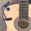 A close-up of a clip-on condenser microphone with a gooseneck attached to an acoustic guitar.