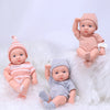 A realistic soft vinyl reborn baby doll with clothes is shown lying on white fluffy material.