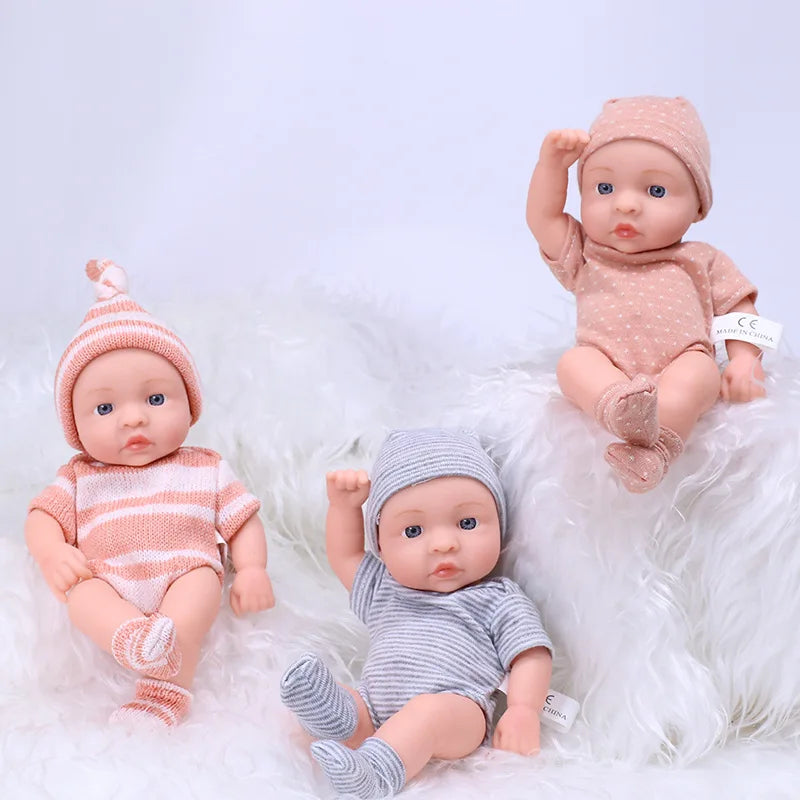 A realistic soft vinyl reborn baby doll with clothes is shown lying on white fluffy material.