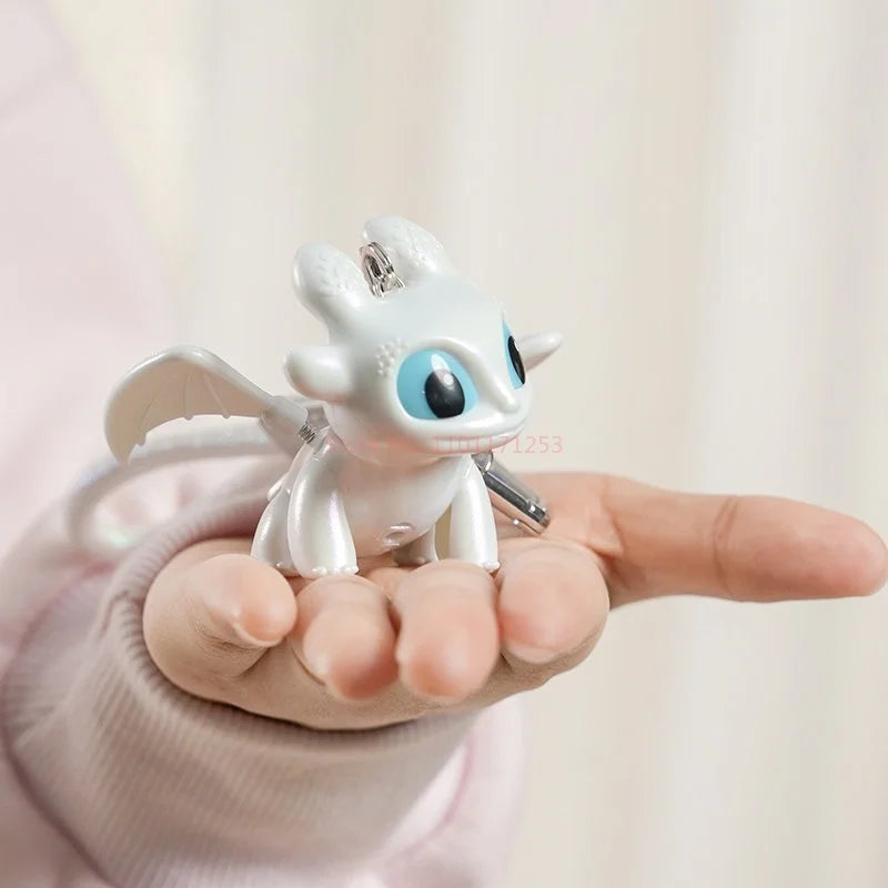 A hand holds a Toothless Dragon keychain with movable wings and glowing eyes against a light background.