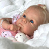 A close-up of an 18-inch lifelike reborn baby doll with hand-rooted hair resting on white fluffy fabric.