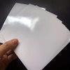 A hand holds a sheet of double-sided diamond painting release paper, showing its glossy white surface.