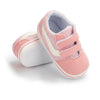 A pair of pink and white striped canvas baby sneakers with soft anti-slip features shown from the side.