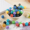 A collection of colorful rhinestone resin bayberry ball beads in various shades and sizes arranged on a light pink dish.