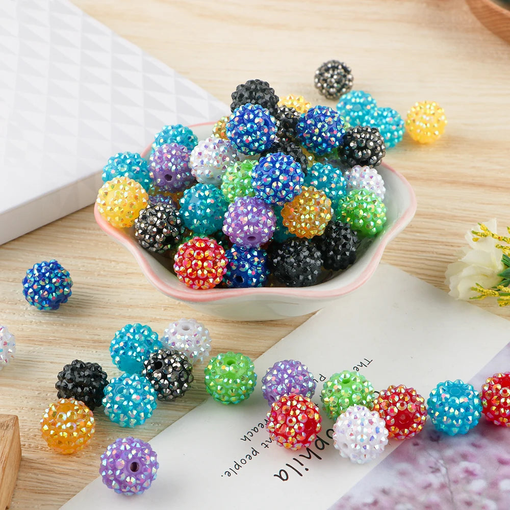 A collection of colorful rhinestone resin bayberry ball beads in various shades and sizes arranged on a light pink dish.