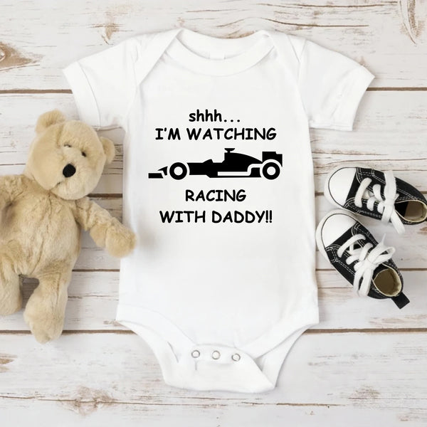 A white baby bodysuit featuring black text that reads Shhh I'm watching racing with daddy