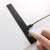 A hand is holding a black LED drawing board with a wire connected to it on a white surface.