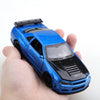 A hand holds a blue die-cast sports car with pull-back action and a roof spoiler.